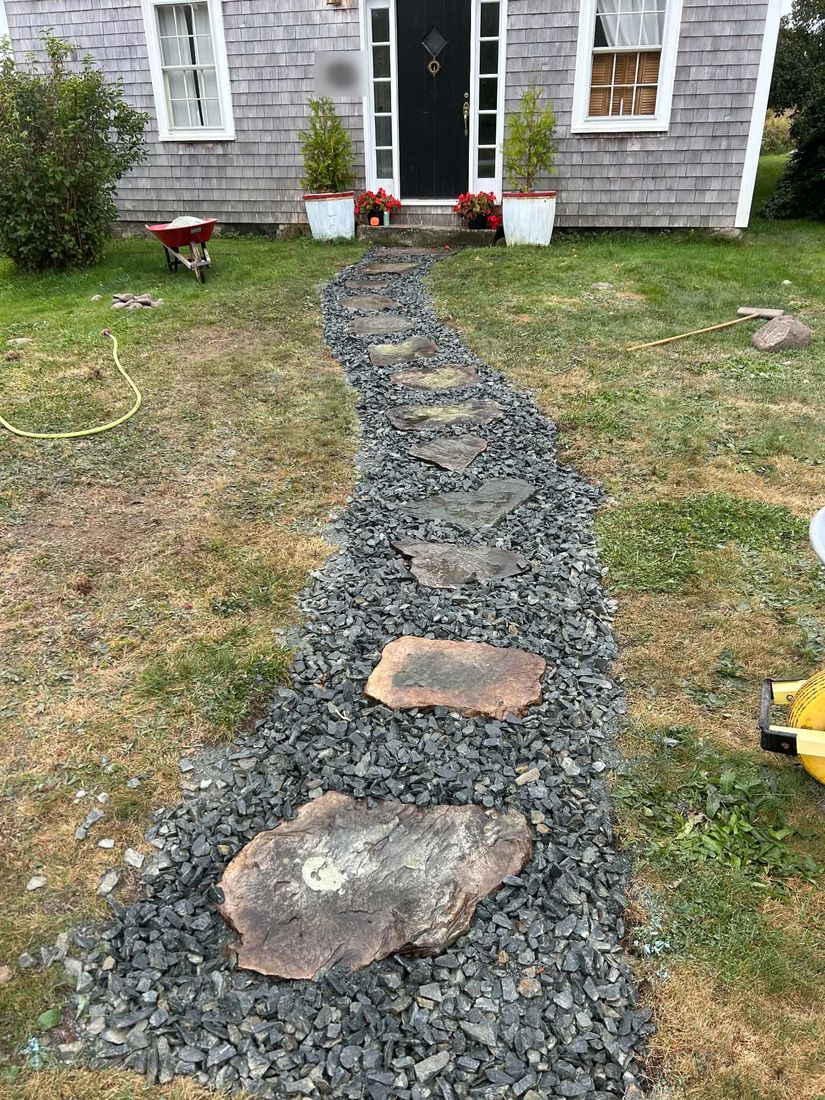 After: a curving path of large flat stepping stones set in dark crushed stone, running across the lawn to the front step of a shingled house